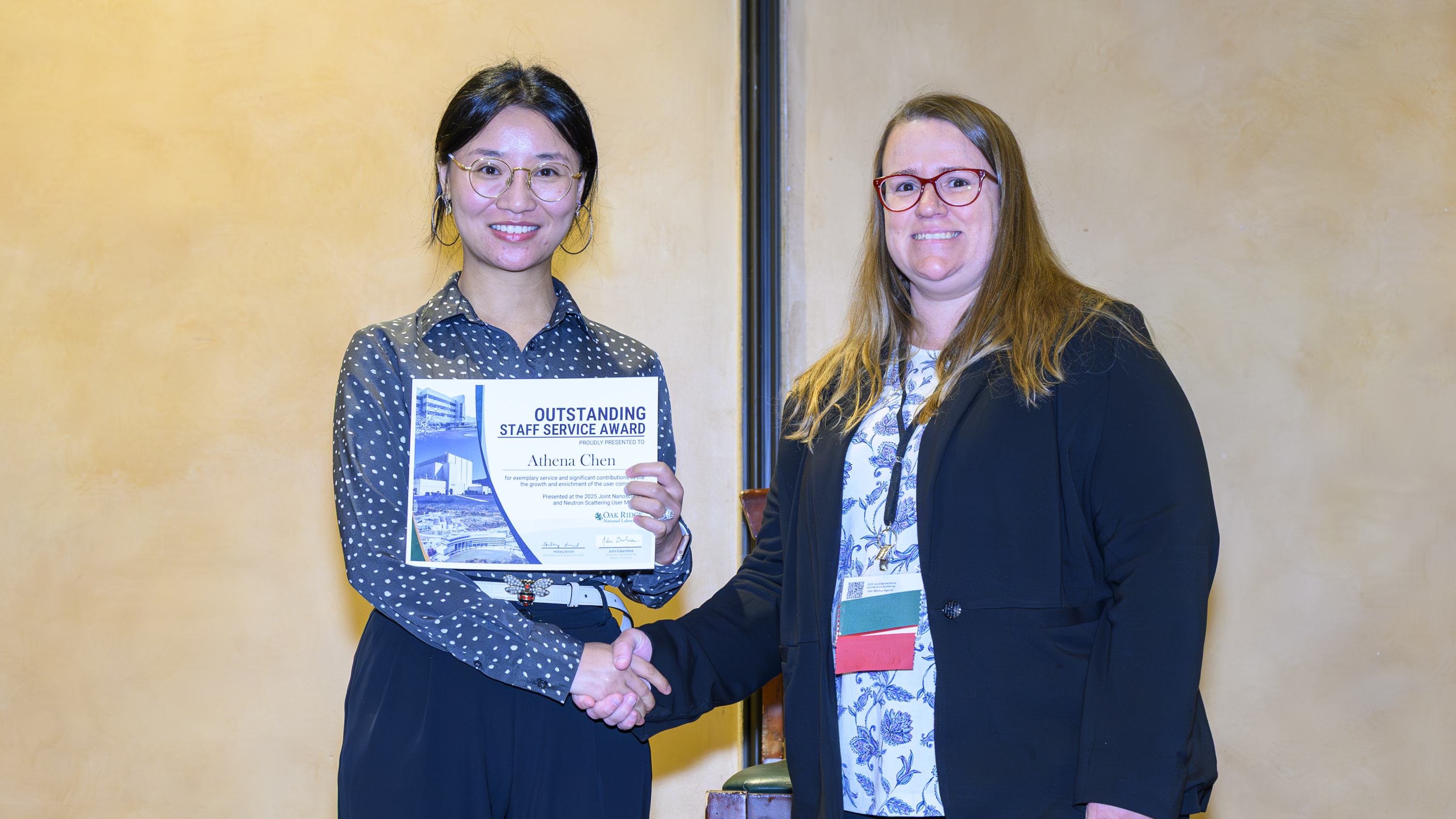 Two women shaking hands. Award winner Athena Chen holding certificate for Outstanding Staff Service Award