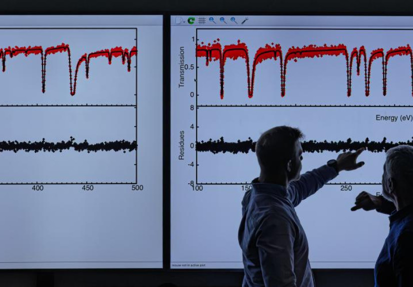 Two researchers analyze spectroscopy graphs on large digital displays in a laboratory setting.