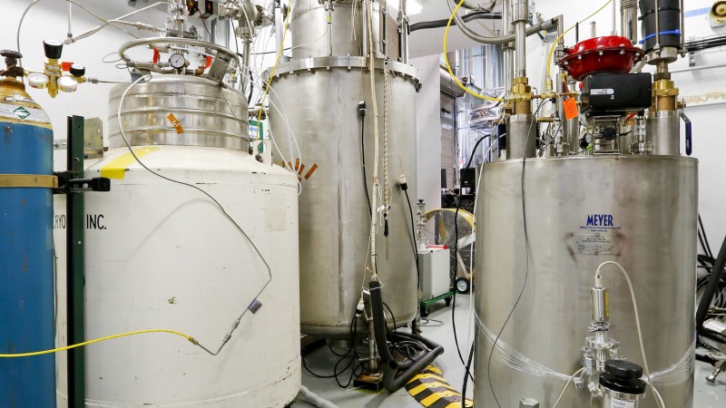 A view of the test environment at the Spallation Neutron Source shows a white tank containing helium on the left, the prototype cryoviscous compressor pump in the middle, and the valve box, which monitors the flow rate to the pump, on the right. Photo: US ITER/ORNL