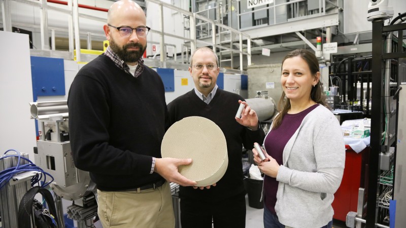 ORNL researchers Todd Toops, Charles Finney, and Melanie DeBusk (left to right) hold an example of a particulate filter used to collect harmful emissions in vehicles. Using neutrons, they are cultivating a better understanding of how heat treatments and oxidation methods can remove layers of soot and ash from these filters, which could lead to improved fuel efficiency. (Image credit: ORNL/Genevieve Martin) 